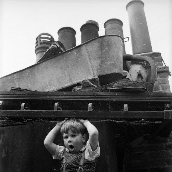 July 1961: A child of the Wapping slums in the East end of London amuses himself amongst the rubbish dumped onto the roof of a building.