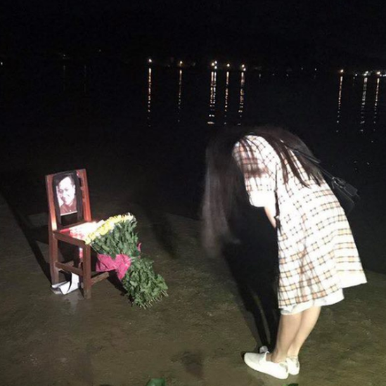 A woman in Guangzhou, China, stands before an empty chair with a photo of Liu Xiaobo and flowers