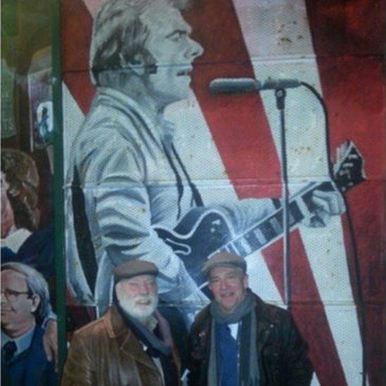 John McCarthy and Brian Keenan next to a mural celebrating Belfast's most famous musician