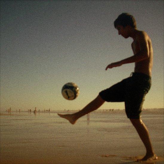 A young man plays football on a beach