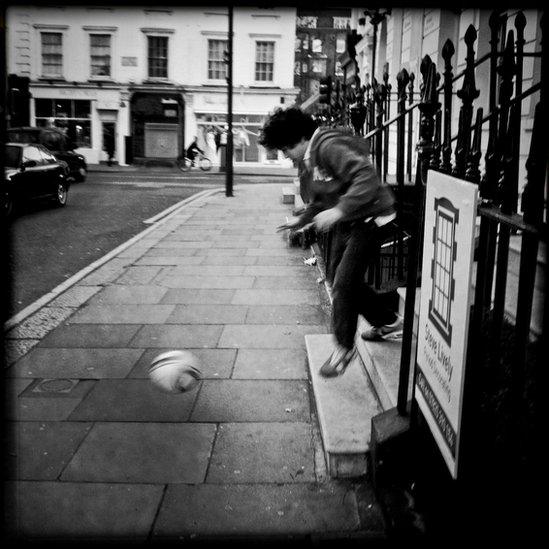 A boy playing with a football in the street
