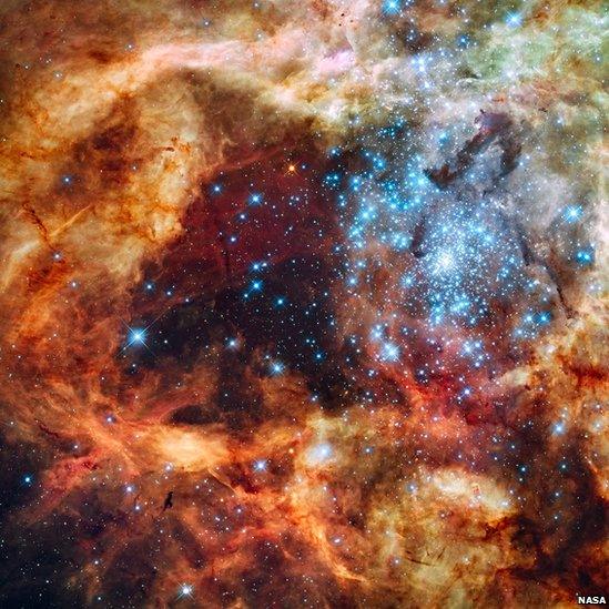 Hubble Space Telescope image - blue stars surrounded by warm, glowing clouds in a nearby stellar nursery