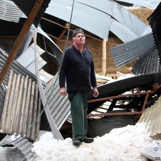 Sheep farmer James McHenry with his lambing shed, which collapsed with the weight of snow over the weekend, killing sheep and lambs at his farm in the Glens of Antrim, Northern Ireland