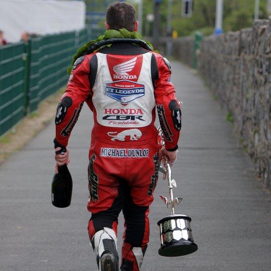 Michael Dunlop leaves the scene of his triumph with a bottle of bubbly and the coveted TT Superbike trophy