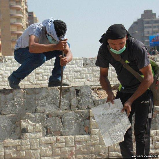 Protesters break up a concrete wall to access the material to throw as missiles at security forces