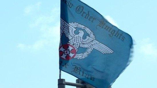 The flag bears the words New Order Knights and Ku Klux Klan