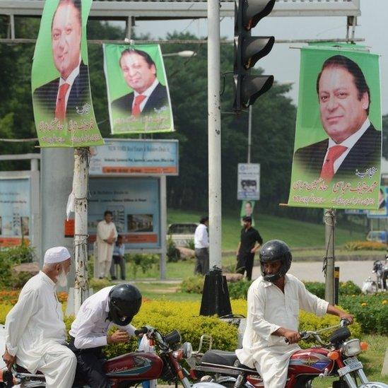 Pakistani commuters wait at the traffic lights alongside a poster of Prime Minister Nawaz Sharif on a highway in Islamabad on August 25, 2014.