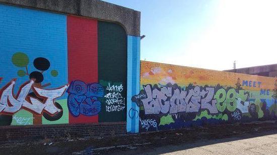 Very colourful murals with graffiti covering much of it along a wall of a bridge