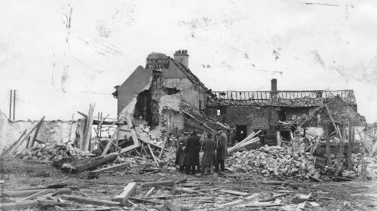 Four people looking at a decimated building after an ammunitions explosion.  The building was the former Railway Hotel in Catterick and photo was taken in 1944. 