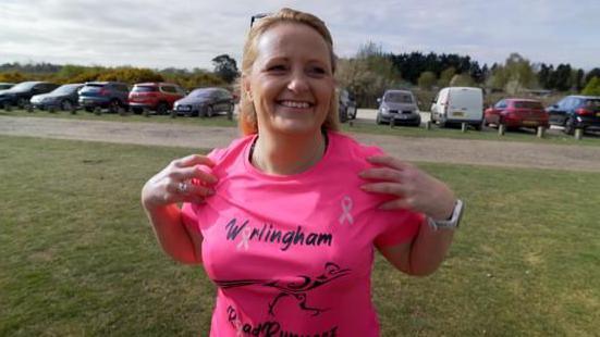Michelle Hewitt, is blonde, and is seen stretching her shoulders at the beginning of the session to warm up. She is wearing a bright pink T-shirt, with the Worlingham RoadRunnerz logo emblazoned on the front.