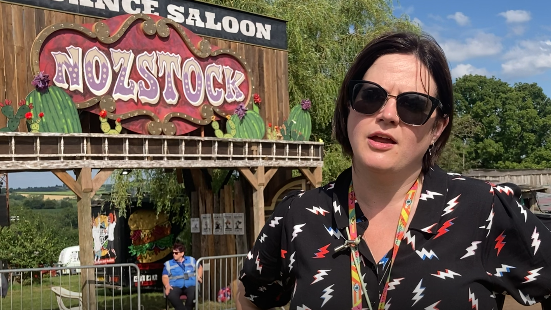 A woman with dark hair and sunglasses stood alongside a structure saying Nozstock