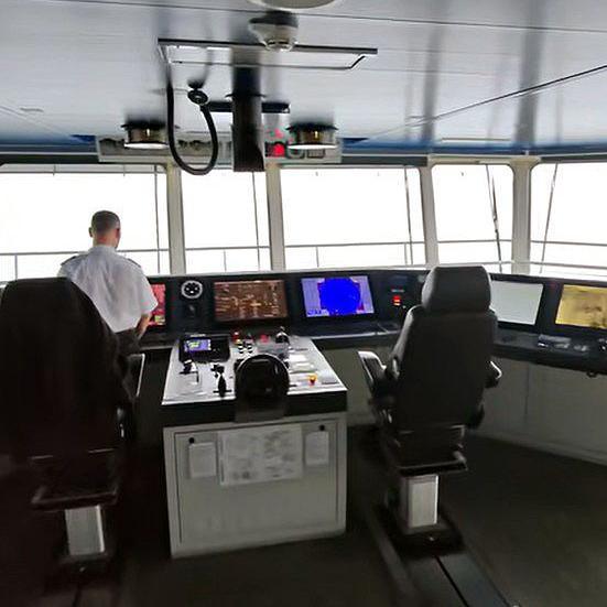 The bridge of a ferry including a member of staff who is being filmed from behind.