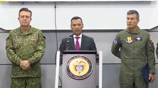 Colombian Defence Minister Pedro Sánchez speaks at a news conference. He is flanked by two high-ranking members of Colombia's military.
The minister is standing at a podium bearing the Ministry of Defence's official seal.