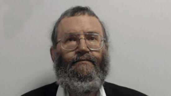 Dr Wayne Davis with brown eyes, grey short hair and long grey beard and glasses in photograph taken by police in custody