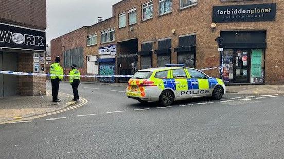 Two police officers guard the scene on Earl Street next to a parked police car.