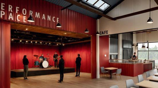 An artist's impression showing a performance space with a low stage and a band playing while three people stand watching them. The area is linked to a cafe, with tables and chairs further away from the stage.