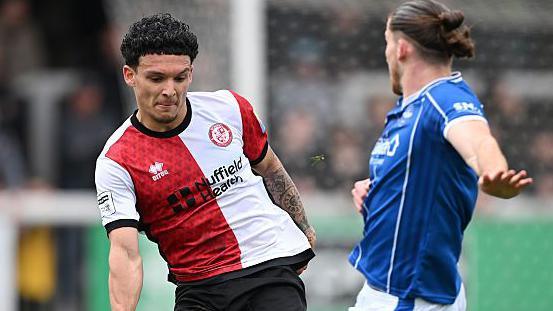 Aaron Drewe of Woking in red and white halved shirt playing against Eastleigh in blue