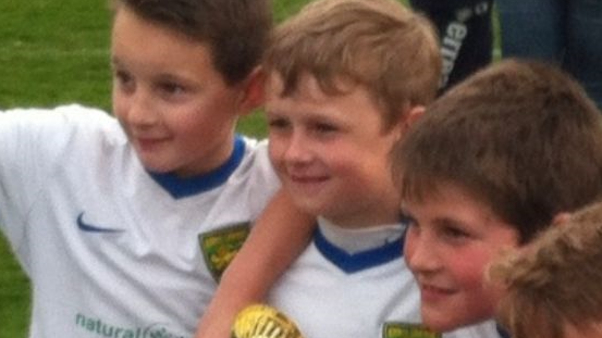 Three boys aged about nine or 10 in white football kits - Joe Dix, Louis Simmons and Tommy Chambers. They are smiling and Louis is holding a trophy. 