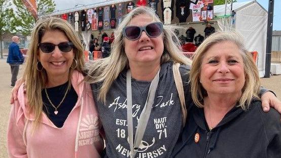Lisa Hymowitz has long blonde hair and is wearing sunglasses and a
pink hoodie. Ivy Capelli has long blonde hair and is wearing sunglasses and a grey jumper. and Amy Magdelin has mid length blonde hair and is wearing a black zip up hoodie.