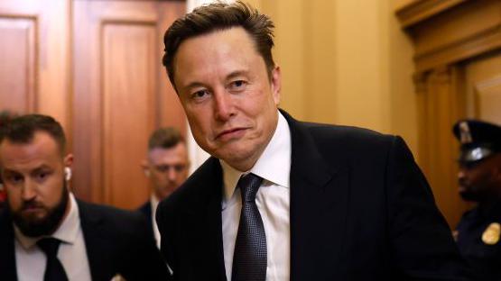 Elon Musk, wearing a suit and holding a coffee, walks through the US Capitol building in Washington 