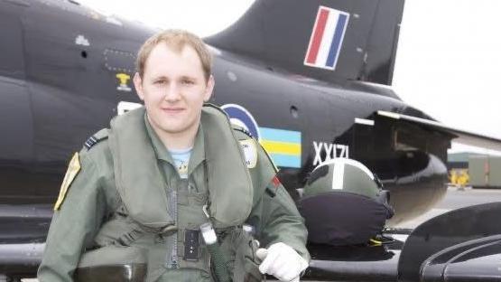 Rob Thomas standing in front of black aircraft in a green jumpsuit