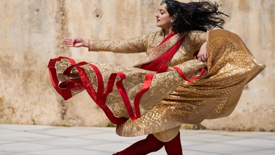 Sonia is mid-performance with traditional dress on. Her clothing is gold and red and floats in the air as she swirls and turns.