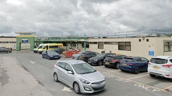 The outpatient entrance and car park with several cars parked alongside the right side of the road