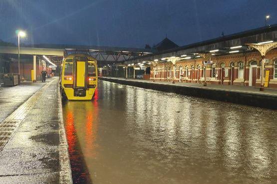 Water flooding the railway tracks at a station. A train is parked on the line.