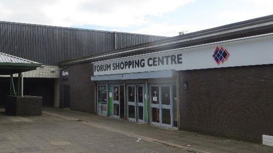 The entrance to a run-down building with a sign over the entrance saying Forum Shopping Centre