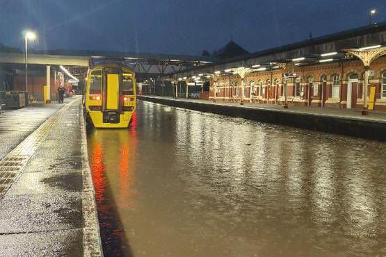 Water flooding the railway tracks at a station. A train is parked on the line.