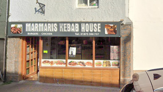 The outside of Marmaris Kebab House with the name written on a grey sign above the brown door and window frames