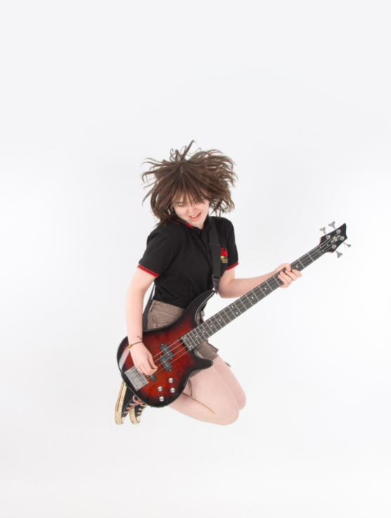 Merch gyda gwallt brown yn neidio gan afael ar gitar trydan.