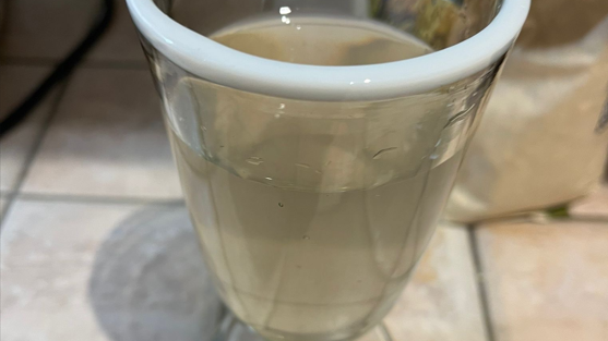 A murky-coloured glass of water can be seen on a kitchen surface