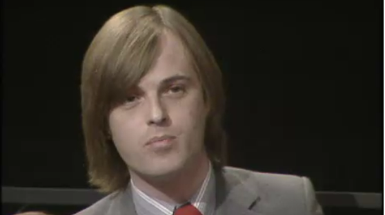 Andrew Smith, with shoulder length hair and a grey suit, talking on the programme.