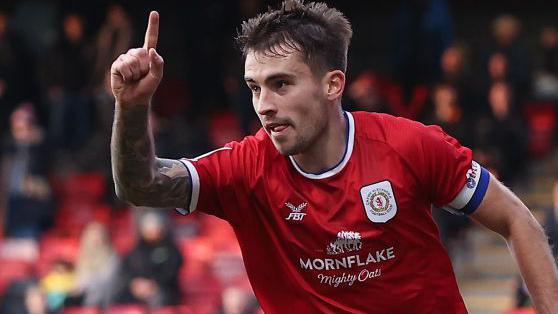 Luke Offord celebrates scoring for Crewe by holding his right arm in the arm and pointing towards the sky with his index finger.