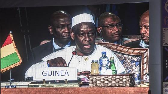 Guinea's former Minister of Defence Mohamed  Diané wearing a white robe and cap, is seen on a giant screen speaking to a microphone. He is flanked by other people behind him during the closing session of a conference gathering defence ministers and officials of 27 African and Arab countries on 25 March, 2016 in Egypt's Red Sea resort town of Sharm el-Sheikh