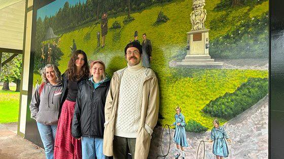 Four artists stand in front of a new mural in the shelter at People's Park in Tiverton