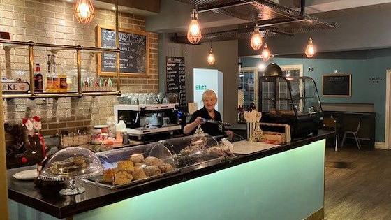 A worker stand behind the counter at the Connections Community Cafe. The counter is lined with cakes.