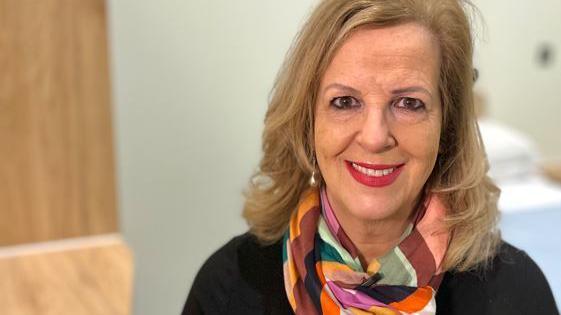 Caroline Donovan smiling while looking directly at the camera. She has long blonde hair and is wearing a black top and multicoloured scarf.