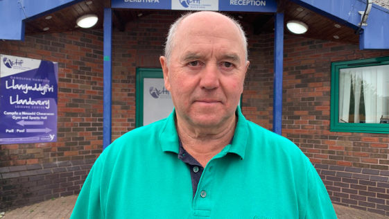 Y Cynghorydd Handel Davies yn sefyll o flaen mynedfa Canolfan Hamdden Llanymddyfri