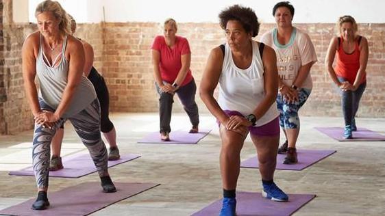 A group of six women in a room stretching. 