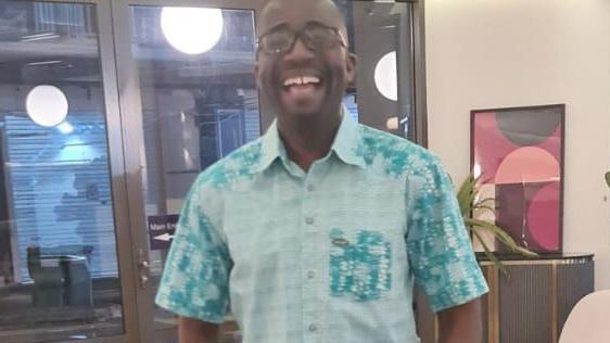 Akwasi is in a lilac short sleeved shirt in an office