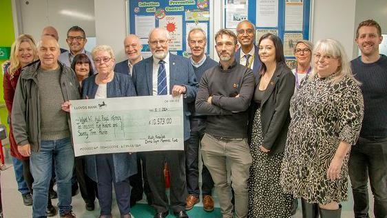 Staff at the unit posing for a photograph with Mrs Knowles, who is dressed in blue and holding a giant cheque.