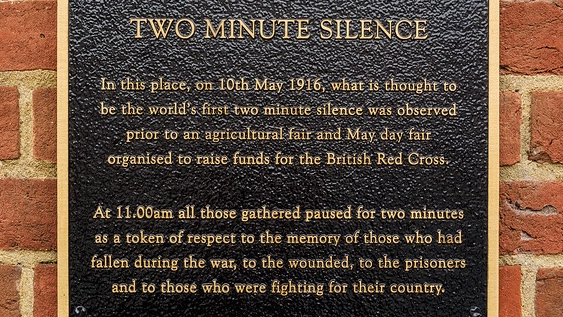 A black plaque with gold writing on a wall marking the world's first two-minute silence in Farnham