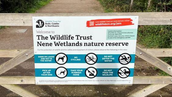 A sign by the Wildlife Trust for Bedfordshire, Cambridgeshire and Northamptonshire which has been put up on a fence at a nature reserve. The sign has rules for visitors including dogs should be kept on leads and not in the water, no cycling and tells people to take their rubbish home.