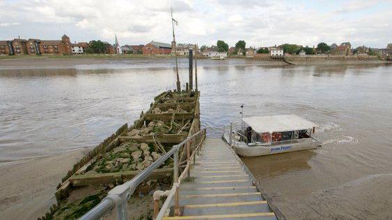 A white boat is docked next to a row of concrete steps, with the wide river beyond it.