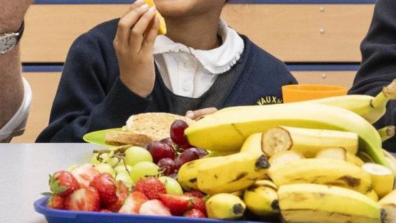 A primary school pupil eating a piece of fruit in front of a tray of fruit at a breakfast club