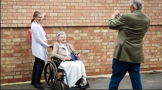 Woman in wheelchair and carer having their photo taken in front of the memorial wall at Bletchley Park