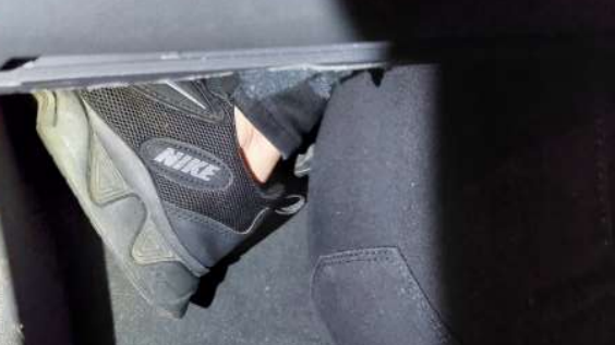 A woman's foot covered in a black Nike trainer sticks out from the glove compartment of a car. 