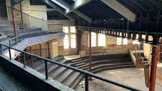 The inside of the building with stepped mouldy seating and peeling walls.